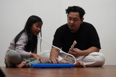 Asyalı bir baba, küçük kızına evde melodi ve kaydedici çalmayı öğreterek, çocuğa müzik aleti tanıtıyor.