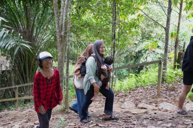 Asyalı Müslüman anne çocuklarıyla birlikte sabahın köründe yemyeşil bir parkta yürüyor. Mutlu bir aile açık hava aktivitesi yapıyor.