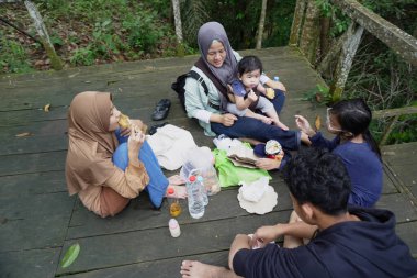 Asyalı Müslüman anne, ormanın ortasında oğlu ve kızıyla piknik yapıyor. Aile bağları kuruyor.