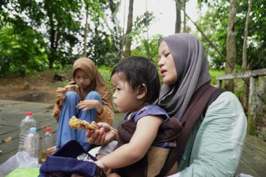 Asyalı Müslüman anne, ormanın ortasında oğlu ve kızıyla piknik yapıyor. Aile bağları kuruyor.