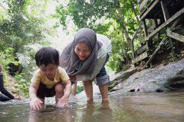 Asyalı Müslüman anne küçük kızıyla bir şelalede oynuyor güneşli bir günün ve açık deniz aktivitelerinin tadını çıkarıyor.
