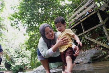 Asyalı Müslüman anne küçük kızıyla bir şelalede oynuyor güneşli bir günün ve açık deniz aktivitelerinin tadını çıkarıyor.