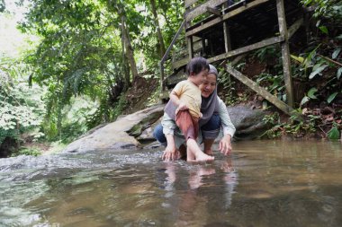 Asyalı Müslüman anne küçük kızıyla bir şelalede oynuyor güneşli bir günün ve açık deniz aktivitelerinin tadını çıkarıyor.