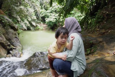 Asyalı Müslüman anne küçük kızıyla bir şelalede oynuyor güneşli bir günün ve açık deniz aktivitelerinin tadını çıkarıyor.