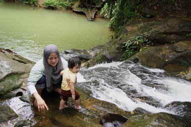 Asyalı Müslüman anne küçük kızıyla bir şelalede oynuyor güneşli bir günün ve açık deniz aktivitelerinin tadını çıkarıyor.