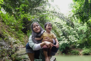 Asyalı Müslüman anne küçük kızıyla bir şelalede oynuyor güneşli bir günün ve açık deniz aktivitelerinin tadını çıkarıyor.