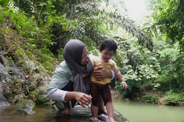 Asyalı Müslüman anne küçük kızıyla bir şelalede oynuyor güneşli bir günün ve açık deniz aktivitelerinin tadını çıkarıyor.