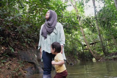 Asyalı Müslüman anne küçük kızıyla bir şelalede oynuyor güneşli bir günün ve açık deniz aktivitelerinin tadını çıkarıyor.