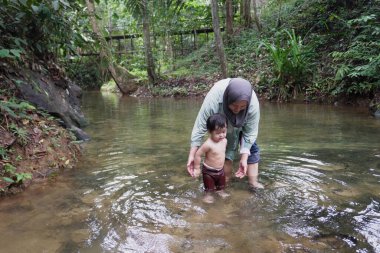 Asyalı Müslüman anne küçük kızıyla bir şelalede oynuyor güneşli bir günün ve açık deniz aktivitelerinin tadını çıkarıyor.