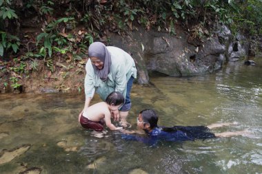 Asyalı Müslüman anne küçük kızıyla bir şelalede oynuyor güneşli bir günün ve açık deniz aktivitelerinin tadını çıkarıyor.