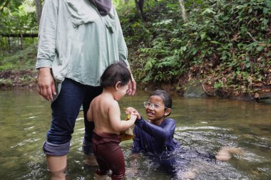 Asyalı Müslüman anne küçük kızıyla bir şelalede oynuyor güneşli bir günün ve açık deniz aktivitelerinin tadını çıkarıyor.