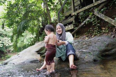 Asyalı Müslüman anne küçük kızıyla bir şelalede oynuyor güneşli bir günün ve açık deniz aktivitelerinin tadını çıkarıyor.