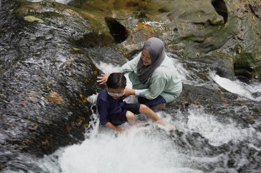 Asyalı Müslüman anne küçük kızıyla bir şelalede oynuyor güneşli bir günün ve açık deniz aktivitelerinin tadını çıkarıyor.