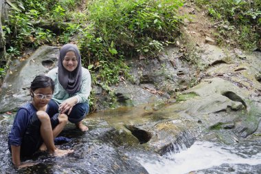Asyalı Müslüman anne küçük kızıyla bir şelalede oynuyor güneşli bir günün ve açık deniz aktivitelerinin tadını çıkarıyor.