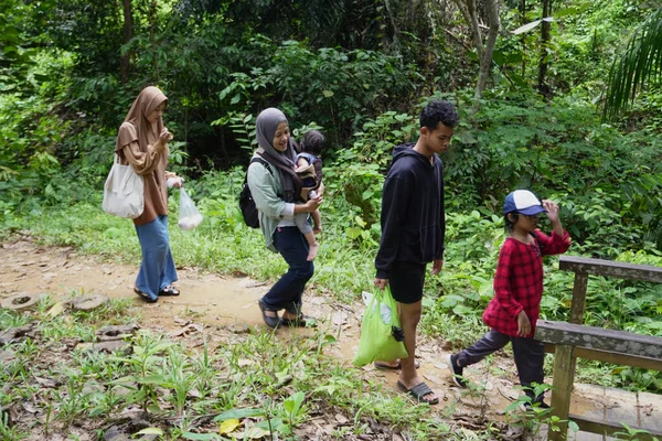 Asyalı Müslüman anne çocuklarıyla birlikte sabahın köründe yemyeşil bir parkta yürüyor. Mutlu bir aile açık hava aktivitesi yapıyor.
