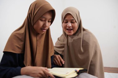 Asyalı Müslüman anne kızına evde Kur 'an okumayı öğretiyor, Arapça yazılar ve Kuran ayetleri öğreniyor.