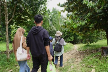 Asyalı Müslüman anne çocuklarıyla birlikte sabahın köründe yemyeşil bir parkta yürüyor. Mutlu bir aile açık hava aktivitesi yapıyor.
