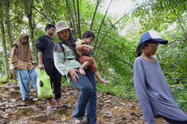 Asyalı Müslüman anne çocuklarıyla birlikte sabahın köründe yemyeşil bir parkta yürüyor. Mutlu bir aile açık hava aktivitesi yapıyor.