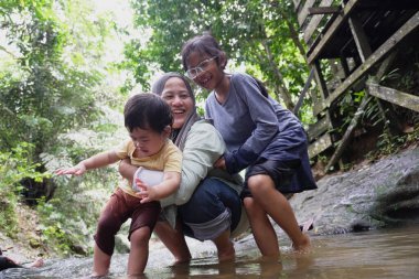 Asyalı Müslüman anne küçük kızıyla bir şelalede oynuyor güneşli bir günün ve açık deniz aktivitelerinin tadını çıkarıyor.