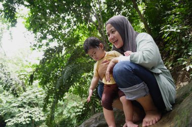 Asyalı Müslüman anne küçük kızıyla bir şelalede oynuyor güneşli bir günün ve açık deniz aktivitelerinin tadını çıkarıyor.
