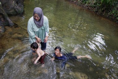 Asyalı Müslüman anne küçük kızıyla bir şelalede oynuyor güneşli bir günün ve açık deniz aktivitelerinin tadını çıkarıyor.