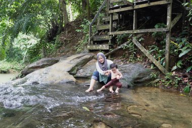 Asyalı Müslüman anne küçük kızıyla bir şelalede oynuyor güneşli bir günün ve açık deniz aktivitelerinin tadını çıkarıyor.