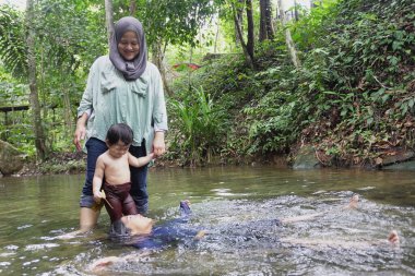 Asyalı Müslüman anne küçük kızıyla bir şelalede oynuyor güneşli bir günün ve açık deniz aktivitelerinin tadını çıkarıyor.