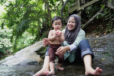 Asyalı Müslüman anne küçük kızıyla bir şelalede oynuyor güneşli bir günün ve açık deniz aktivitelerinin tadını çıkarıyor.