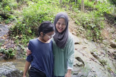 Asyalı Müslüman anne küçük kızıyla bir şelalede oynuyor güneşli bir günün ve açık deniz aktivitelerinin tadını çıkarıyor.