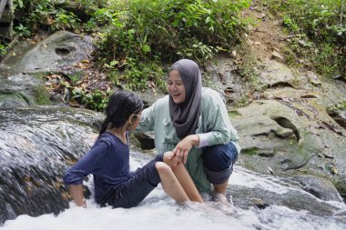 Asyalı Müslüman anne küçük kızıyla bir şelalede oynuyor güneşli bir günün ve açık deniz aktivitelerinin tadını çıkarıyor.