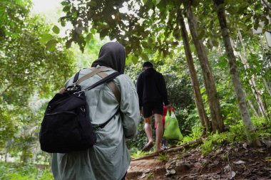 Asyalı Müslüman anne çocuklarıyla birlikte sabahın köründe yemyeşil bir parkta yürüyor. Mutlu bir aile açık hava aktivitesi yapıyor.