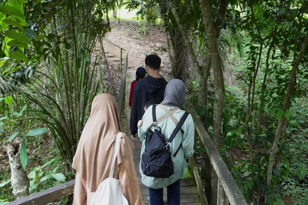 Asyalı Müslüman anne çocuklarıyla birlikte sabahın köründe yemyeşil bir parkta yürüyor. Mutlu bir aile açık hava aktivitesi yapıyor.