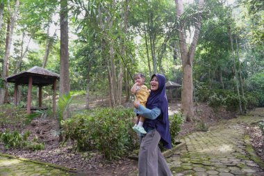 Mutlu Asyalı Müslüman anne küçük kızıyla yürüyor ve oynuyor büyük ağaçların altında, Woodland Park 'ta, sabah aktiviteleri