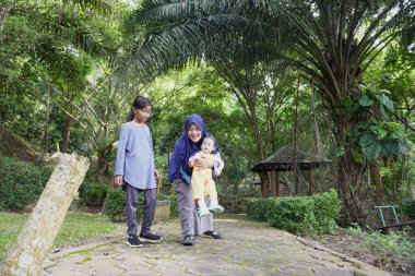 Mutlu Asyalı Müslüman anne küçük kızıyla yürüyor ve oynuyor büyük ağaçların altında, Woodland Park 'ta, sabah aktiviteleri