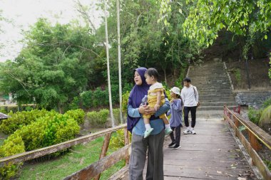 Zengin bir orman parkında ahşap bir köprüde yürüyen mutlu Asyalı anne ve çocuklar güneşli bir sabah yürüyüşü ve aile doğası gezintisinin keyfini çıkarıyorlar.