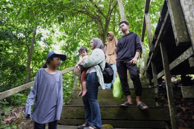 Zengin bir orman parkında ahşap bir köprüde yürüyen mutlu Asyalı anne ve çocuklar güneşli bir sabah yürüyüşü ve aile doğası gezintisinin keyfini çıkarıyorlar.