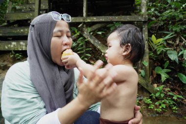Mutlu Asyalı Müslüman anne tesettüre girip çocuklarıyla temiz bir orman nehrinde güneşli bir günde banyo yapıyor. Aile bağları doğada, açık havada yaz etkinliklerinde.