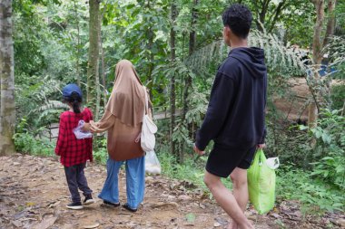 Doğada piknik, gençlik macerası ve açık hava yaşam tarzı için yiyecek paketleri taşıyan, ormanda kirli bir yolda yürüyen mutlu genç Asyalı kardeşler.