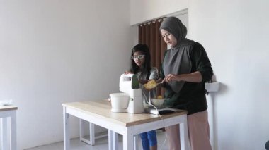 Asyalı Müslüman anne kızıyla pasta yapıyor, aile yemeği kavramı, elektrikli mikserde hamuru karıştırıyor.
