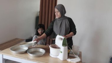 Asyalı Müslüman anne kızıyla pasta yapıyor, aile yemeği kavramı, elektrikli mikserde hamuru karıştırıyor.