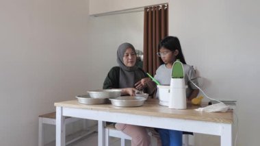 Asyalı Müslüman anne kızıyla pasta yapıyor, aile yemeği kavramı, hamuru pişirme tavasına döküyor.