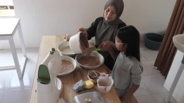 Asyalı Müslüman anne kızıyla pasta yapıyor, aile yemeği kavramı, hamuru pişirme tavasına döküyor.