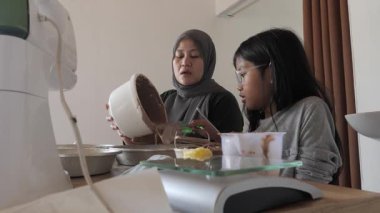 Asyalı Müslüman anne kızıyla pasta yapıyor, aile yemeği kavramı, hamuru pişirme tavasına döküyor.