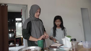 Asyalı Müslüman anne kızıyla pasta yapıyor, aile yemeği kavramı, krem şanti ile pasta süsleme.