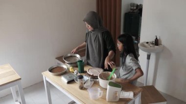 Asyalı Müslüman anne kızıyla pasta yapıyor, aile yemeği kavramı, krem şanti ile pasta süsleme.
