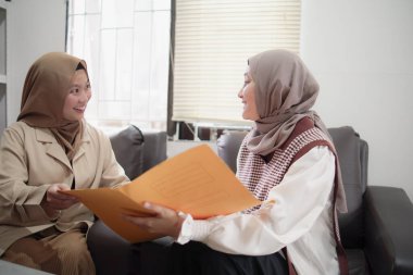 İki güzel Asyalı genç Müslüman iş kadını ofiste oturmuş iş projelerini, mesleki işbirliği ve kadın güçlendirme kavramını tartışıyorlar.