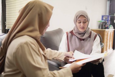 İki güzel Asyalı genç Müslüman iş kadını modern bir ofiste çalışırken gülümseyen bir klasörde belgeleri tartışıyor.