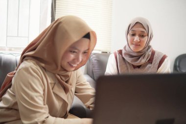 Modern bir ofis, profesyonel işbirliği ve dijital yaşam tarzında dizüstü bilgisayarda birlikte çalışan iki güzel Asyalı Müslüman iş kadını.