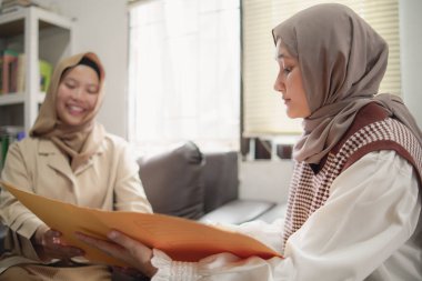 İki güzel Asyalı genç Müslüman iş kadını modern bir ofiste çalışırken gülümseyen bir klasörde belgeleri tartışıyor.