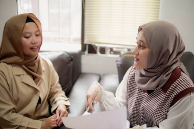 İki güzel Asyalı genç Müslüman iş kadını ofiste oturmuş iş projelerini, mesleki işbirliği ve kadın güçlendirme kavramını tartışıyorlar.